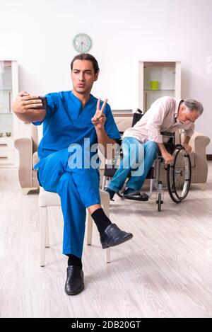 Alter Mann im Rollstuhl und schlechter Betreuer drinnen Stockfoto