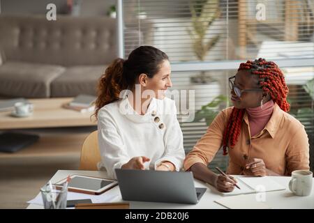 Porträt von zwei lächelnden Geschäftsfrauen diskutieren Projekt, während am Schreibtisch sitzen zusammen und arbeiten an Startup im Büro, Copy Space Stockfoto