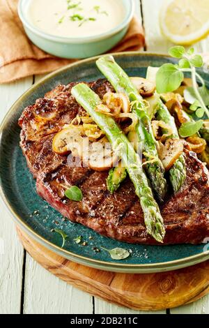 Gegrilltes Rumpsteak mit frischen grünen Spargelfrüchten und mit frischen Kräutern und Gewürzen garnierten Pilzen in Nahaufnahme Stockfoto