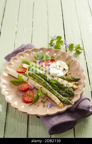 Verschiedene frische grüne und weiße Spargel-Triebe mit Kräutern bestreut und mit cremigem Dressing und Scheiben Erdbeeren im hohen Winkel mit Co serviert Stockfoto