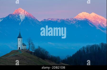 LETZTE AMPEL AUF DEN KAMNIK-SAVINJA ALPEN (STORŽIČ GIPFEL AUF DER LINKEN SEITE) MIT DER KIRCHE ST. PRIMOŽ, JAMNIK. Stockfoto