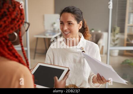 Taille up Porträt der erfolgreichen Geschäftsfrau im Gespräch mit weiblichen Praktikanten und lächelnd fröhlich, während im Büro Innenraum stehen, kopieren Raum Stockfoto