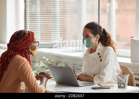 Porträt einer Managerin, die Maske trägt, während sie eine junge afroamerikanische Frau im Büro interviewt, Raum kopieren Stockfoto