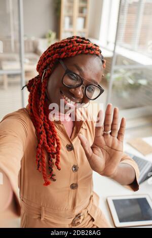 Hochwinkelporträt einer jungen afroamerikanischen Frau, die vor der Kamera winkt Während der Aufnahme von Selfie-Fotos oder Live-Streaming aus dem Home Office Stockfoto