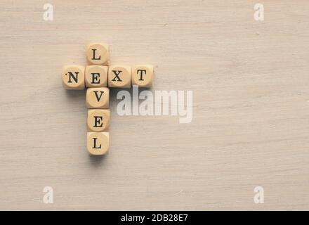 Die Worte auf der nächsten Ebene auf kleinen Holzblöcken auf einem Holztisch mit Platz für Text Stockfoto