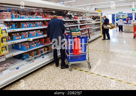 Covid 19 Tesco Supermarkt Innenlager Picker mit Trolley Auswahl Lebensmittel Lebensmittel aus den Regalen für Online-Lebensmitteleinkauf Heimtransporter Lieferung Großbritannien Stockfoto