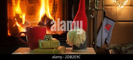 Tasse heiße Schokolade oder Kaffee, Geschenke und Weihnachtsgnome auf Vintage-Holz-Tisch vor Kamin als Hintergrund. Stockfoto