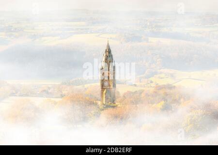 Abberley Uhrenturm (Mini Big Ben), Worcestershire, Großbritannien, im Morgennebel, während die aufgehende Herbstsonne durch das Tal strömt. Stimmungsvolle Szene. Stockfoto