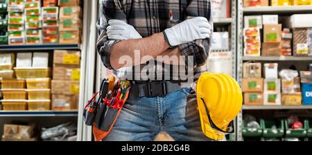 Tischlerelektriker im Laden von elektrischen Bauteilen mit verschränkten Armen trägt er Schutzhandschuhe. Bauindustrie, Elektrik. Stockfoto