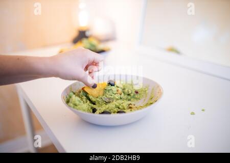 Weibliche Hand Dipping Nachos in Guacamole Sauce mit Oliven Stockfoto