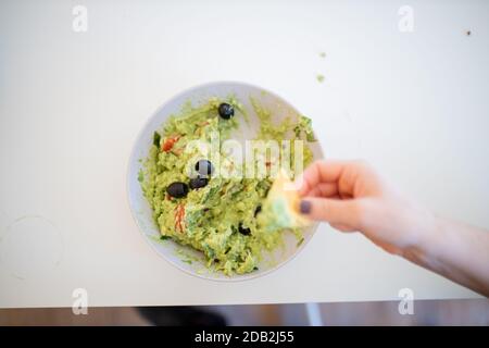 Weibliche Hand Dipping Nachos in Guacamole Sauce mit Oliven Stockfoto