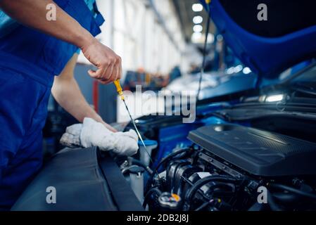 Arbeiter in Uniform überprüft den Motorölstand, Car Service Station. Automobil-Prüfung und Inspektion, professionelle Diagnose und Reparatur Stockfoto