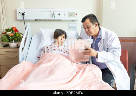 Zuversichtlich asiatischen Arzt Erklärung zu fröhlichen weiblichen Patienten auf medizinischen Zustand liegen auf dem Bett im Krankenhaus. Stockfoto