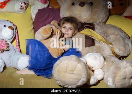 Ein kleines Mädchen in einem blauen Kleid liegt in einem Haufen von großen Plüsch Spielzeug Stockfoto