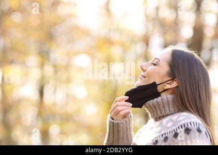 Seitenansicht Porträt einer zufriedenen Frau beim Abheben Schutzmaske zum Einatmen frischer Luft in der Herbstsaison Ein Park Stockfoto