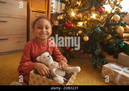 Portrait von glücklichen afroamerikanischen Mädchen Eröffnung Weihnachtsgeschenke, während sitzen am Baum zu Hause und lächeln an der Kamera, kopieren Raum Stockfoto