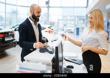 Weibliche Verkäufer gibt Schlüssel von neuem Auto zu Mann in Autohaus. Kunde und Verkäuferin im Fahrzeugraum, Mann, der Transport kauft, Automobil Stockfoto