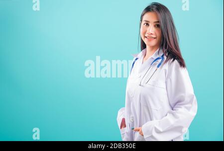 Portrait asian Beautiful Doctor Woman lächelte sie stehend mit Händen in Taschen auf blauem Hintergrund, mit Kopierraum für Text Stockfoto
