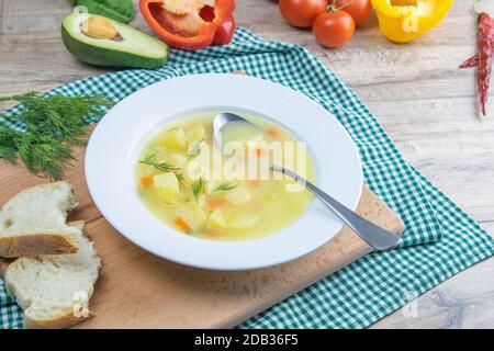 Weiße Milchsuppe mit Kartoffeln, Karotten, Gemüse steht in einem weißen Teller auf einem Holzbrett. Stockfoto