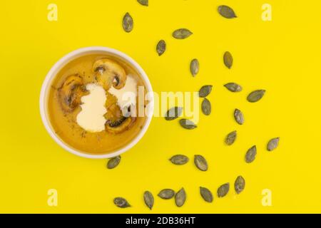 PEA Suppe mit Pilzen in einem rosa Teller steht auf einem gelben Hintergrund, Kürbiskerne sind verstreut. Stockfoto