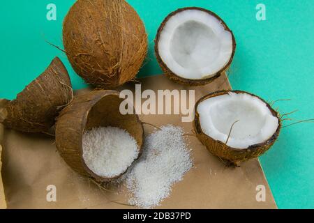 Zerbrochene Kokosnüsse auf Papier, das auf einem türkisfarbenen Hintergrund steht, neben verstreuten Kokosspäne. Stockfoto