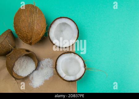 Zerbrochene Kokosnüsse auf Papier, das auf einem türkisfarbenen Hintergrund steht, neben verstreuten Kokosspäne. Stockfoto