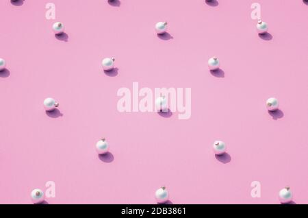 Silber matt Weihnachtskugeln regelmäßig auf rosa Hintergrund verteilt. Weihnachtsschmuck mit Schatten auf strukturierter Oberfläche. Stockfoto