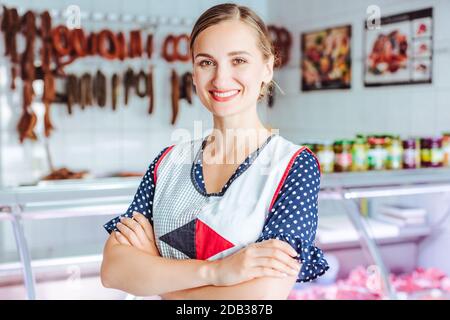 Stolze Frau, die Fleisch und Würstchen in Metzgerei stehend Arme gefaltet verkauft Stockfoto