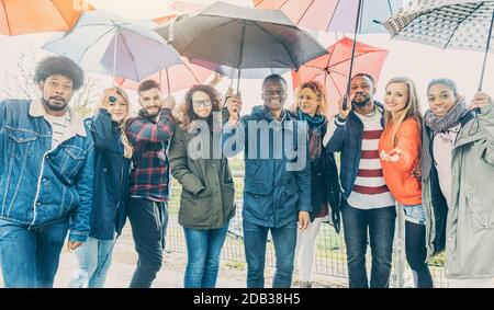 Freunde, die das Beste aus Regen und schlechtem Wetter unter Regenschirmen stehen Stockfoto