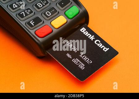 Nahaufnahme eines Zahlungsterminals mit Kreditkarte. Modernes Gerät zur Bezahlung von Dienstleistungen und Waren auf orangefarbenem Hintergrund. Geld von einem abschreiben Stockfoto
