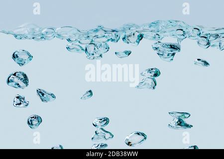 Vollformatansicht aufsteigender Luftblasen im Medium Wasser vor hellblauem Hintergrund. Stockfoto