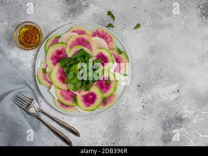 Gesunder veganer Salat aus Wassermelone Rettich und Rucola auf einem Teller. Heller Beton- oder Steinhintergrund. Draufsicht, Kopierraum Stockfoto