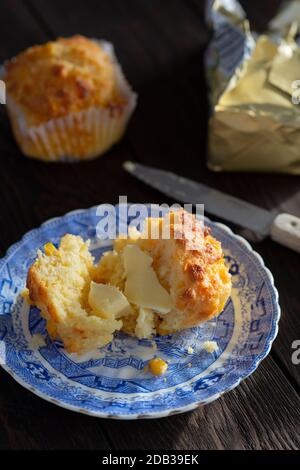 Maisbrot-Muffins mit Cheddar-Käse und Butter auf einem blauen Vintage-Teller auf einem Holzhintergrund - FOODPIX Stockfoto