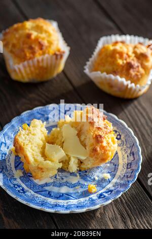 Maisbrot-Muffins mit Cheddar-Käse und Butter auf einem blauen Vintage-Teller auf einem Holzhintergrund - FOODPIX Stockfoto