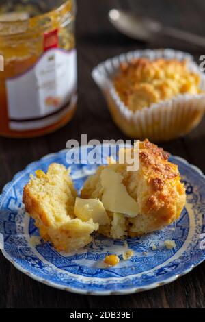 Maisbrot-Muffins mit Butter und Obstmarmelade auf einem blauen Vintage-Teller auf einem Holzhintergrund - FOODPIX Stockfoto