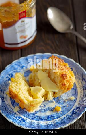 Maisbrot-Muffins mit Butter und Obstmarmelade auf einem blauen Vintage-Teller auf einem Holzhintergrund - FOODPIX Stockfoto