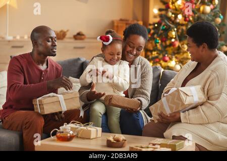 In warmen Farbtönen Porträt der glücklichen afroamerikanischen Familie Eröffnung Weihnachtsgeschenke während Genießen Sie die Weihnachtszeit zu Hause Stockfoto