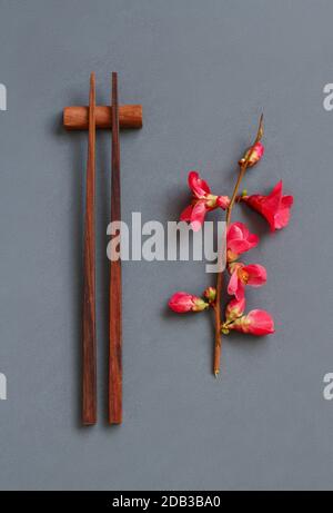 Essstäbchen und rosafarbene Blumen auf grauem Grund. Japanisches Lebensmittelkonzept Stockfoto