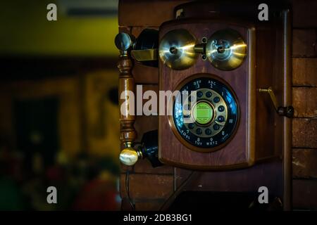 Altes altmodisches Telefon für Wandmontage an der Wand aus Backstein, mit Griff und Kurbel aus Holz und Messing, Messingglocken und Wähltasten, verschwommener Hintergrund Stockfoto