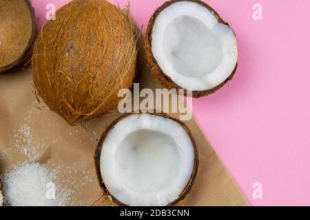 Gebrochene Kokosnüsse auf Bastelpapier, das auf einem rosa Hintergrund steht. Stockfoto