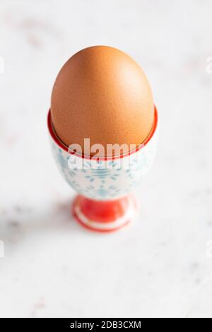 Gekochtes Ei im farbenfrohen blauen und roten Eierbecher mit Löffel auf weißem Marmorhintergrund – FOODPIX Stockfoto
