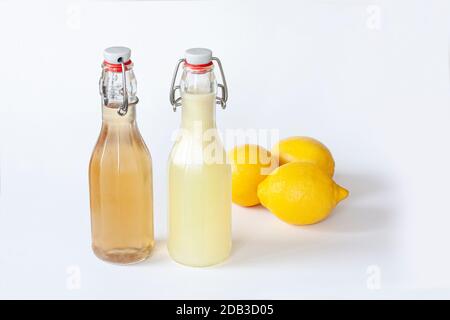 Zwei Flip-Top-Lackschließflaschen mit hausgemachtem Zitronensaft oder Zitronensaft und drei Zitronen auf weißem Hintergrund. Stockfoto