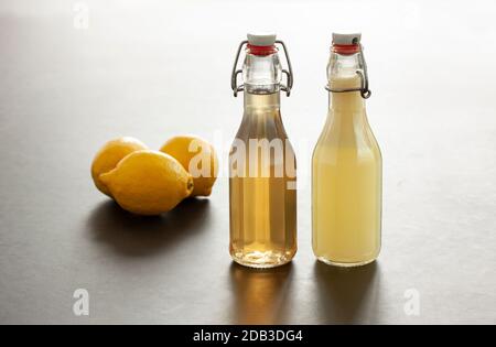 Zwei Flip-Top-Lackschließflaschen mit hausgemachtem Zitronensaft oder Zitronensaft und drei Zitronen im Hintergrund. Teilweise hintergrundbeleuchtetes Studiobild mit Reflectio Stockfoto