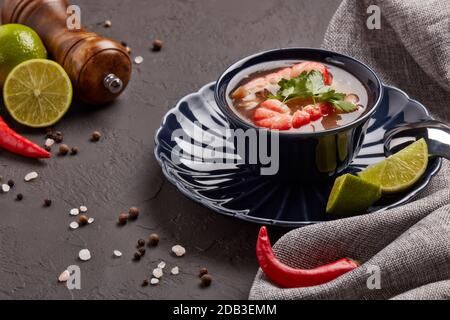 Köstliche Fischsuppe mit Garnelen in dunkelblauer Schale serviert mit Gewürzen und Limette auf dunkelgrauem Hintergrund. Gesunde Ernährung. Meeresfrüchtekarte Stockfoto