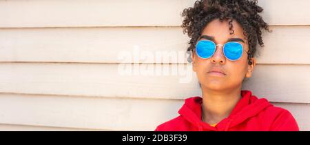 Panorama Mädchen Teenager cool teen gemischt Rasse biracial afrikanisch amerikanisch Weibliche junge Frau trägt eine blaue Sonnenbrille und einen roten Hoodie Im Sommerurlaub Stockfoto