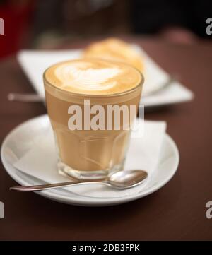 Flacher weißer Kaffee aus transparentem Glas mit weißem Schaum, Essen auf dem Tisch in einem Café Stockfoto