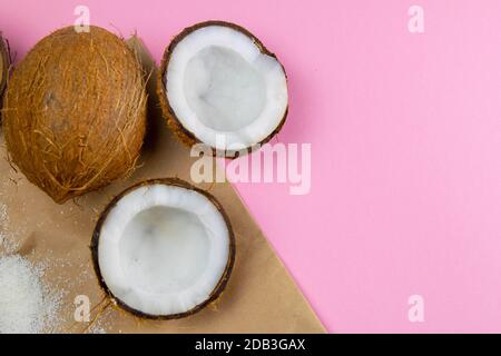 Gebrochene Kokosnüsse auf Bastelpapier, das auf einem rosa Hintergrund steht. Stockfoto