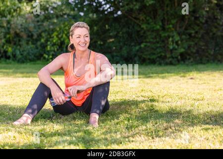 Outdoor-Porträt einer attraktiven mittleren Alters blonde Frau lächelnd Trinkwasser entspannend nach dem Training, Laufen, Yoga oder Fitness-Lifestyle Stockfoto