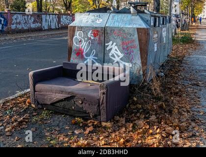 Container für Müllabfuhr und verlassene alte Sofa auf dem Bürgersteig In Berlin Mitte Stockfoto