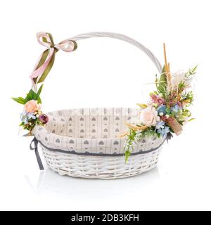 Weißer Korbkorb mit Ziergewebe im Inneren. Dekoriert mit verschiedenen Blumen in zarten Farben, isoliert auf weißem Hintergrund Stockfoto